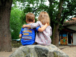Zwei Kinder sitzen auf einem Stein, mit dem Rücken zur Kamera