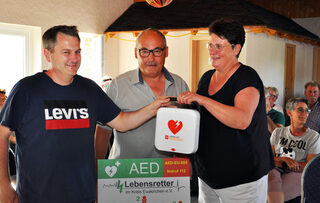 Andreas Schmitz vom Verein „Lebensretter im Kreis Euskirchen“ (links) übergibt den Defibrillator AEDs an den Vorsitzenden der Dorfgemeinschaft Wahlen, Ralf Klöckner, und dessen Stellvertreterin Gabi Lang.