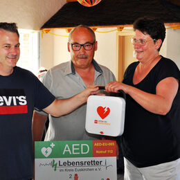 Andreas Schmitz vom Verein „Lebensretter im Kreis Euskirchen“ (links) übergibt den Defibrillator AEDs an den Vorsitzenden der Dorfgemeinschaft Wahlen, Ralf Klöckner, und dessen Stellvertreterin Gabi Lang.
