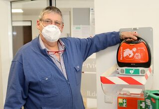 Harald Heinen mit dem Defibrillator, der im Vorraum des Kaller Rathauses hängt. Außerhalb der Rathausöffnungszeiten ist das Gerät derzeit nicht verfügbar.