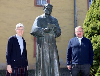 Pater Lambertus Schildt und Schwester Helene Engelmayer neben der Statue von Pater Jordan vor dem alten Gästehaus in Steinfeld.