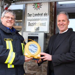 Direkt am Rathaus befindet sich einer der vier Defibrillatoren, die im Gemeindegebiet installiert wurden, wie Bürgermeister Hermann-Josef Esser (rechts) und Wehrleiter Harald Heinen demonstrieren.