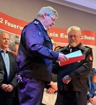Hauptfeuerwehrmann Reiner Züll ist seit 60 Jahren im Löschzug Kall aktiv: Gemeindewehrleiter Harald Heinen (links) übergibt ihm die Gold-Auszeichnung des Verbandes der Feuerwehren in Nordrhein-Westfalen.