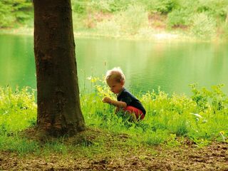 Kind im der Natur vor einem Baum und Wasser im Hintergrund